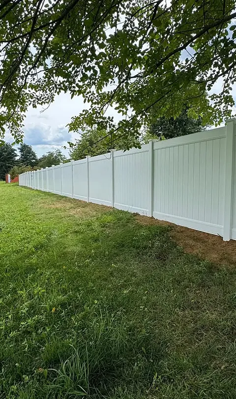 A long, white vinyl fence installed under a shady tree